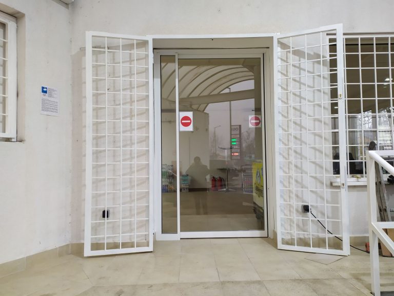 Fehér biztonsági ajtórács egy üvegezett bejárati ajtó előtt